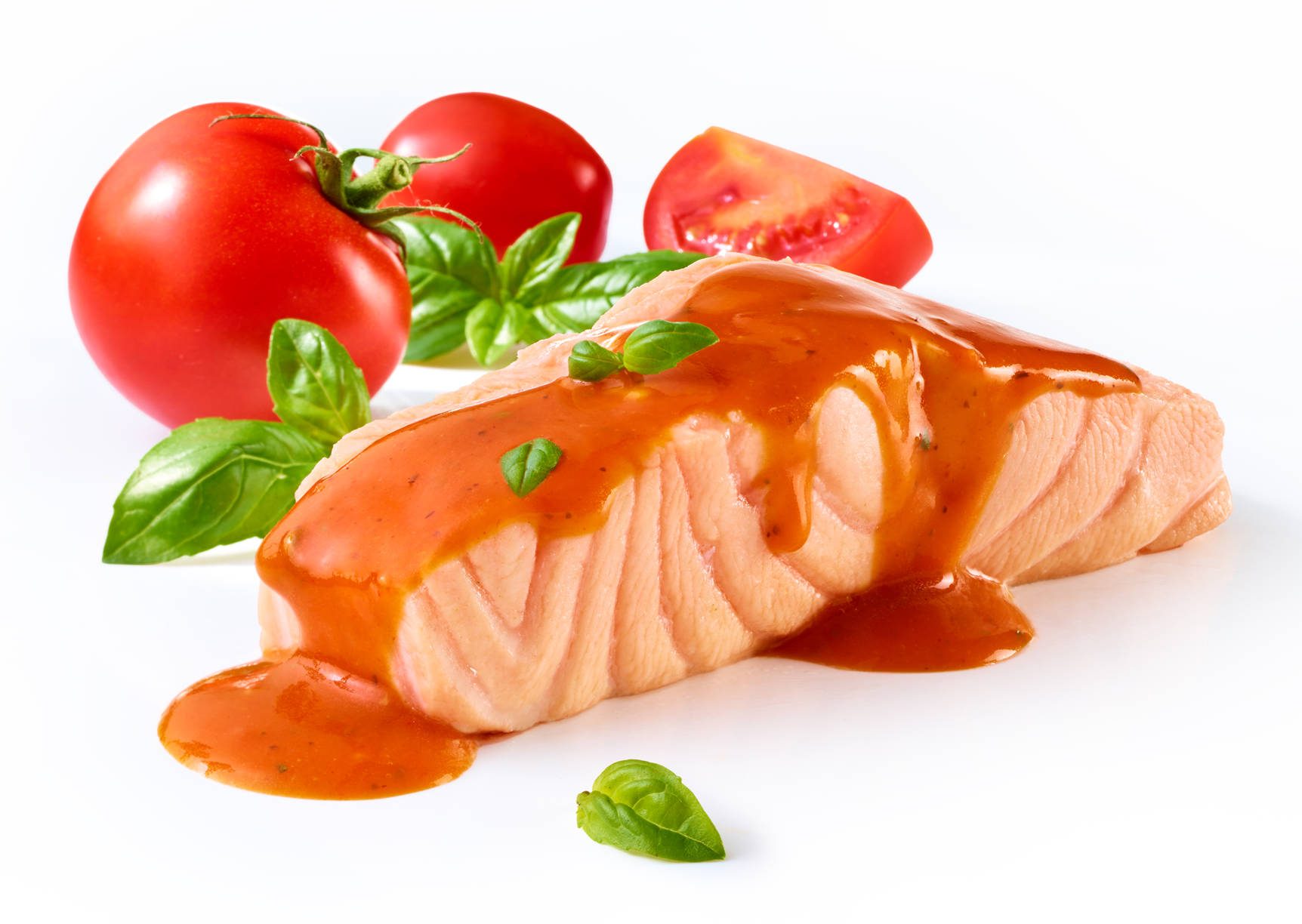 Ein Stück frisch gegarter, saftiger Lachs mit roter Soße, Tomate und Basilikumblättern. Auf weißem Untergrund.