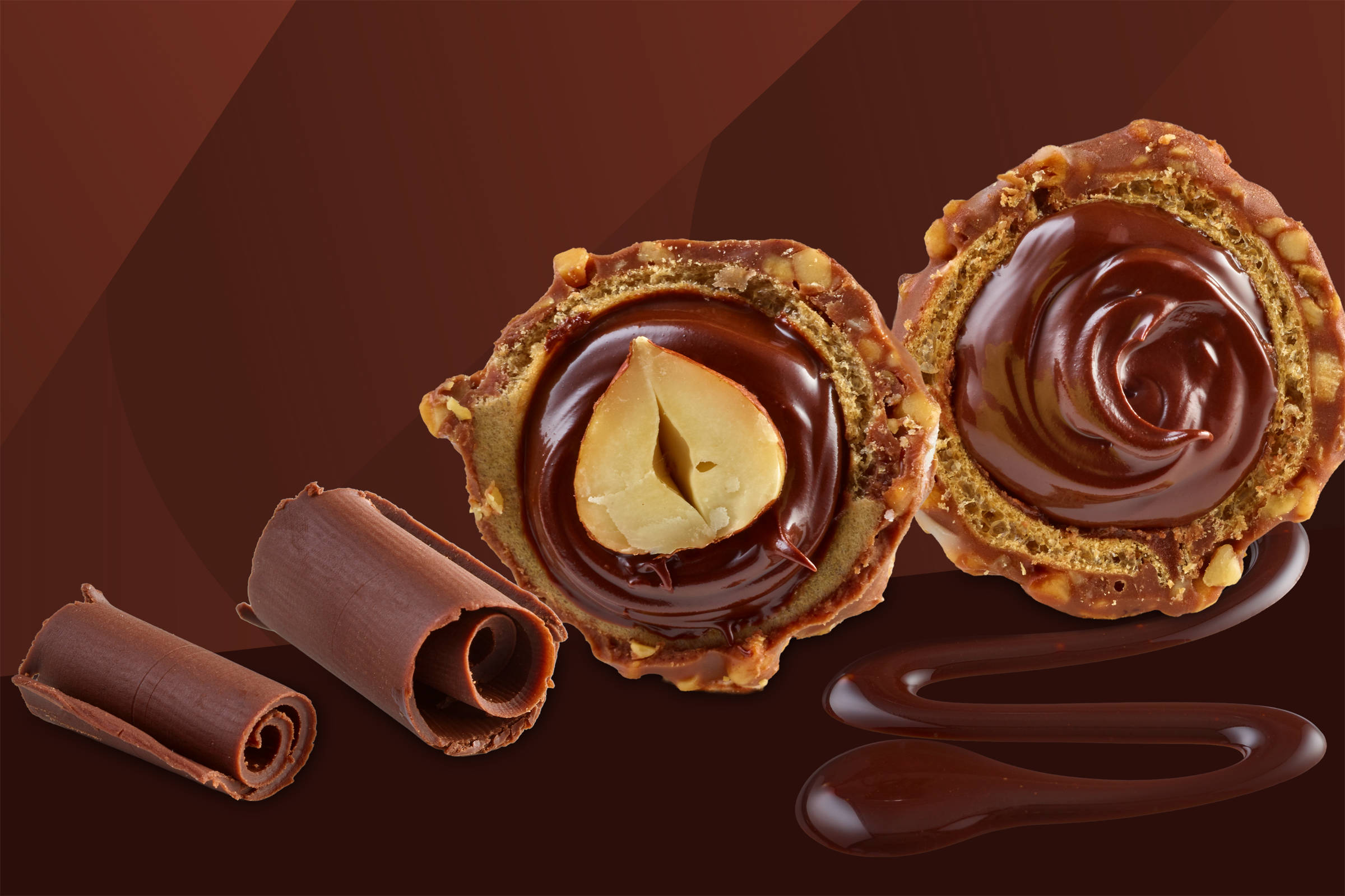 Praline: zwei Rollen hauchdünner Schokolade neben einer halbierten Praline mit ganzer Haselnuss in der Mitte, Krokant.