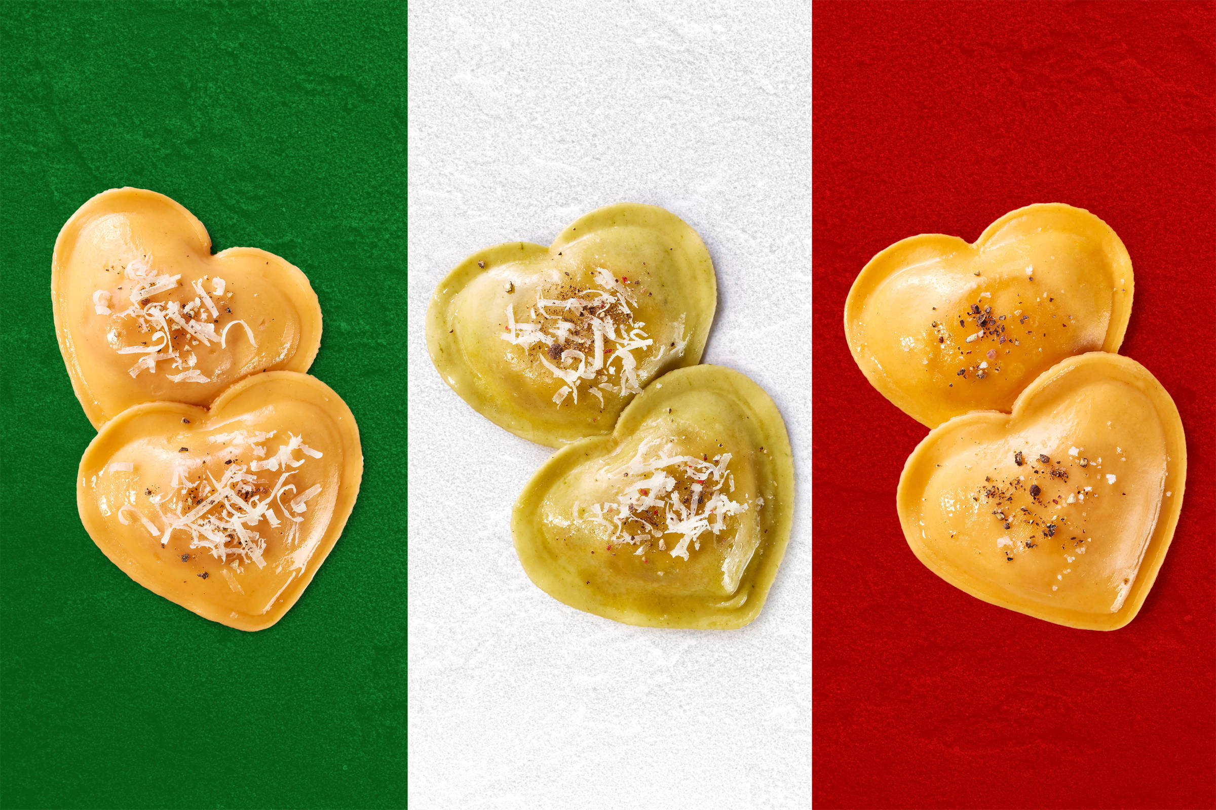 3x Pasta in Herzform vor den drei Farben der itaienischen Flagge: grün, weiß, rot fotografiert und mit etwas Parmesan bestreut.