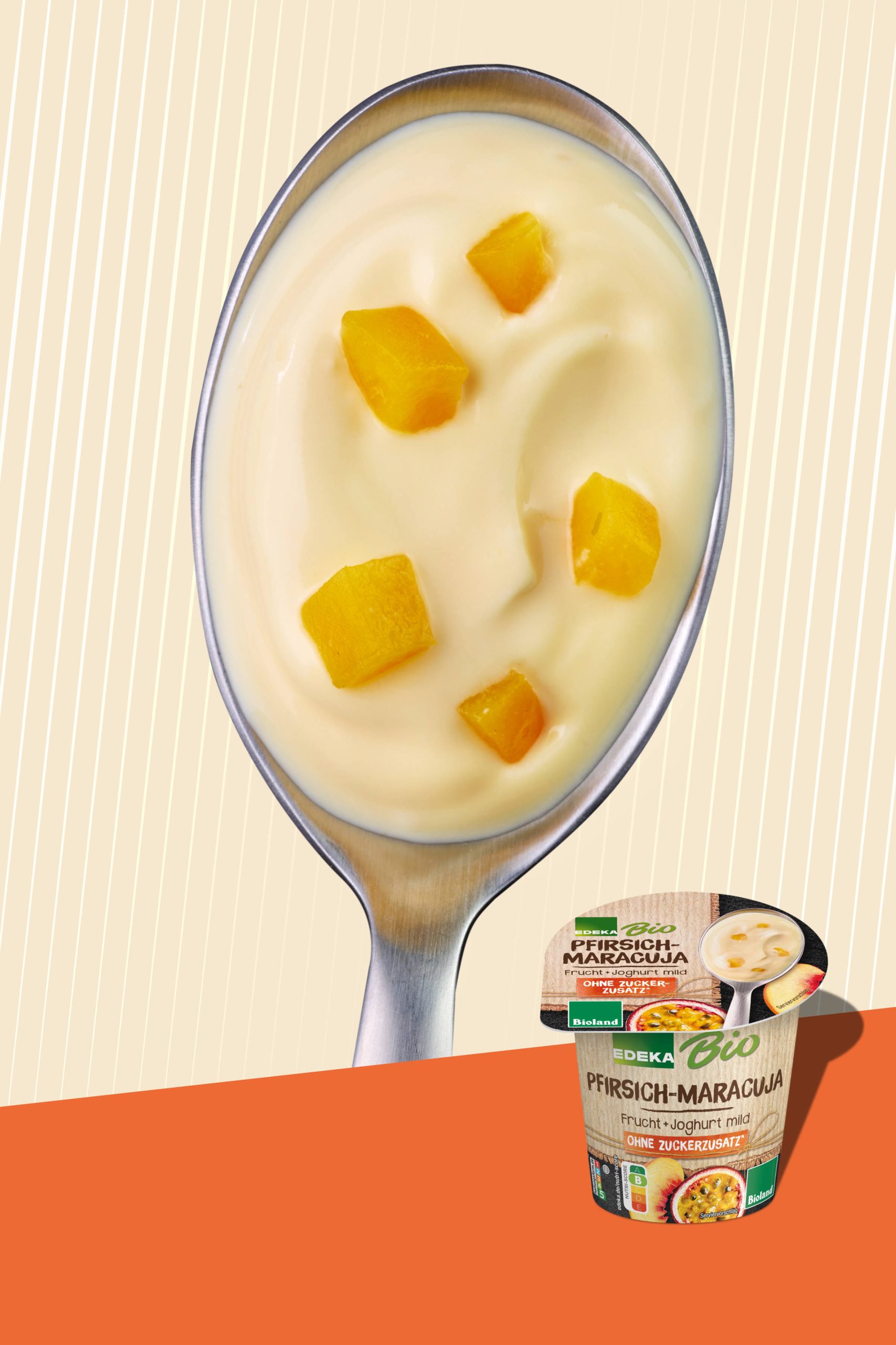 Ein Löffel mit Pfirsich-Maracuja Joghurt und Fruchtstücken auf hellem gestreiftem Hintergrund. Das untere Drittel ist orange und zeigt die Verpackung des Edeka Bioland Joghurts.